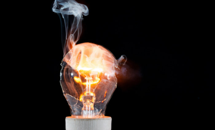 A cracked and burnt out lightbulb on fire with a black background