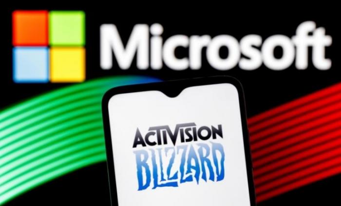 Image of Microsoft logo with a phone screen showing Activision Blizzard over the top to represent the acquisition. 