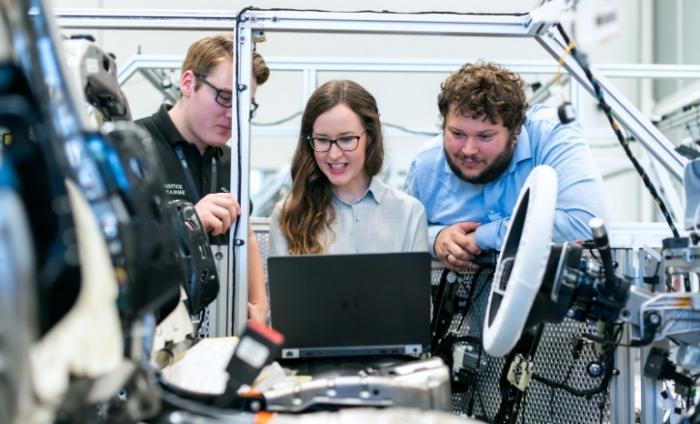 Photo of two men and one woman gathered around a laptop in a car manufacturing plant.